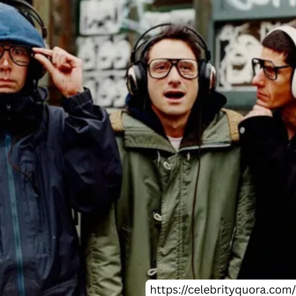 The Beastie Boys, including Ad-Rock, are shown wearing headphones in front of a backdrop that includes their name.