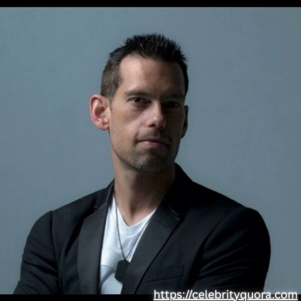 A close-up portrait of Tom Bilyeu wearing a black jacket over a white shirt and a necklace.
The background is a solid grey, with "The Jay Kim Show" logo visible in the lower right corner.