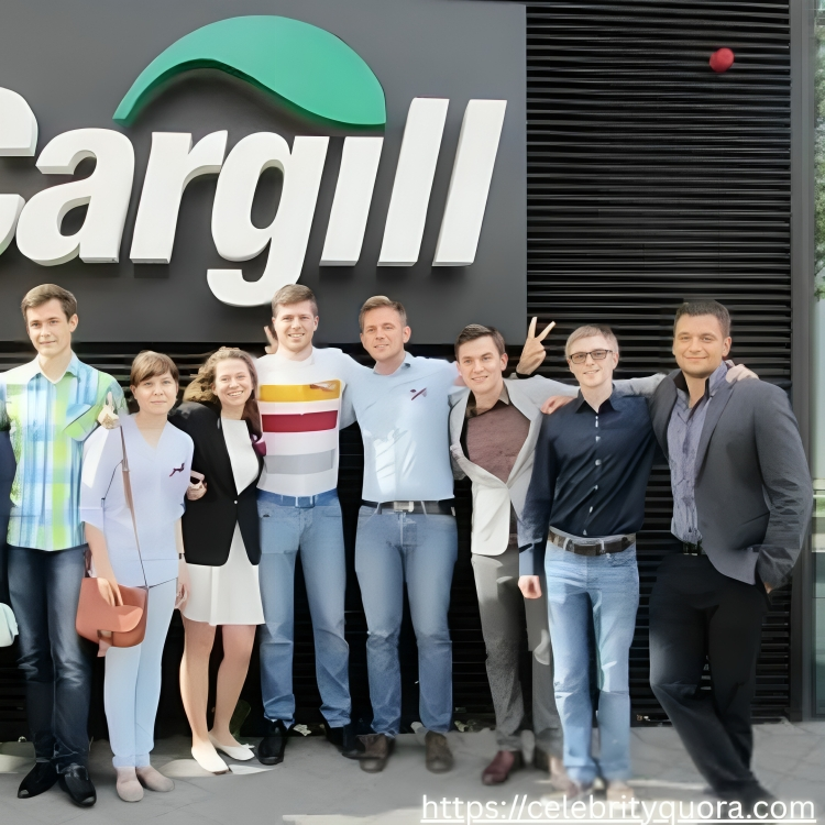 A group of ten young adults poses outdoors in front of a building with the "Cargill" logo. They are standing on a paved surface, smiling, and dressed in casual and business-casual attire.