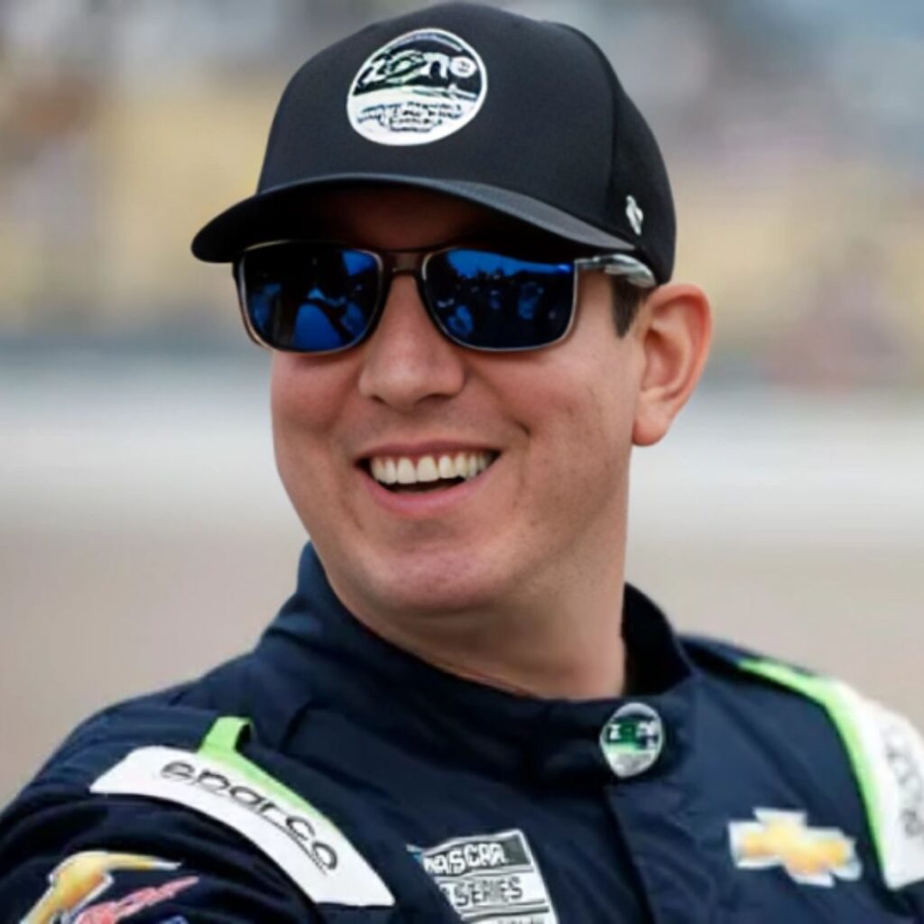 A headshot of Kyle Busch smiling at night, wearing his yellow M&M's sponsored firesuit.
