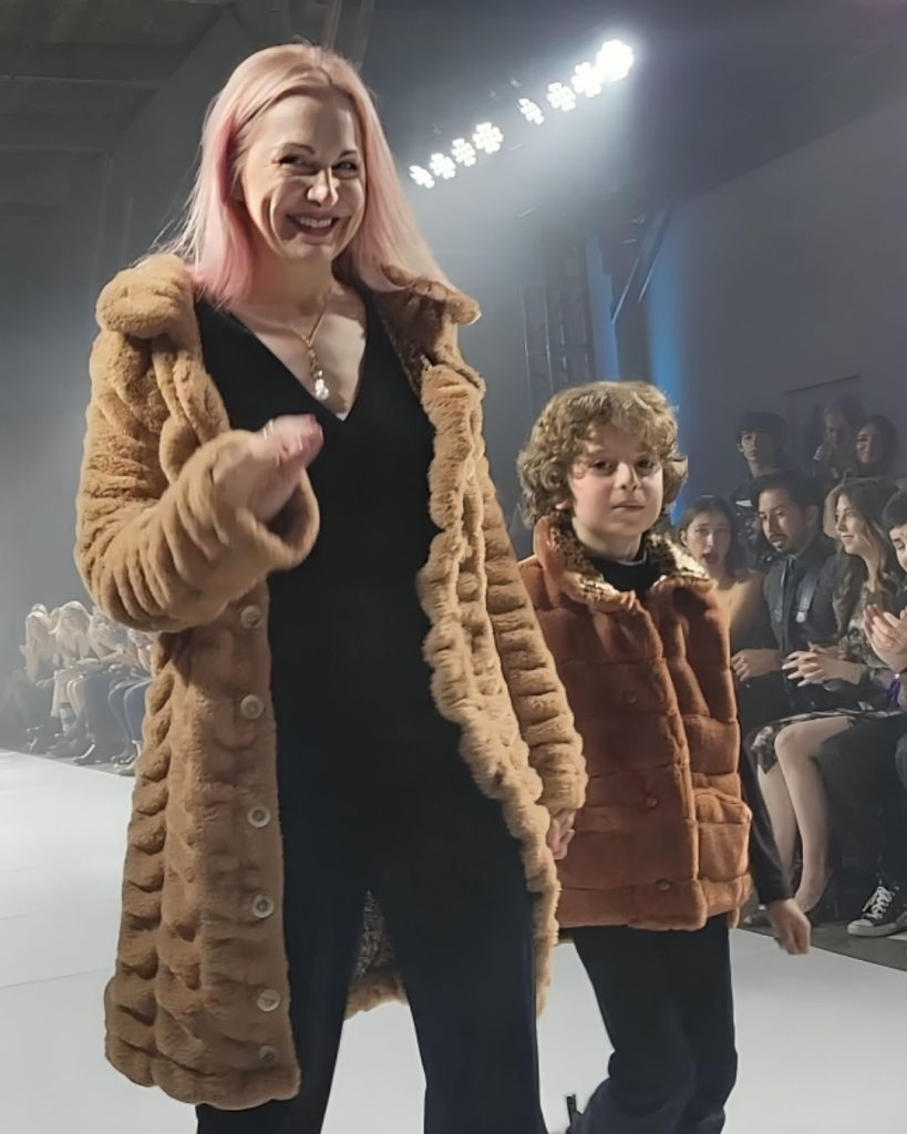 Max Alexander and his mother walking down a runway together, both wearing fur coats.