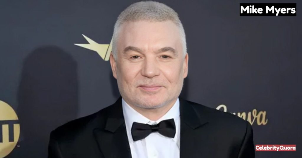 A headshot of actor Mike Myers, who has short, silvery-white hair and is wearing a classic black tuxedo with a black bow tie. He is looking directly at the camera with a slight smile.