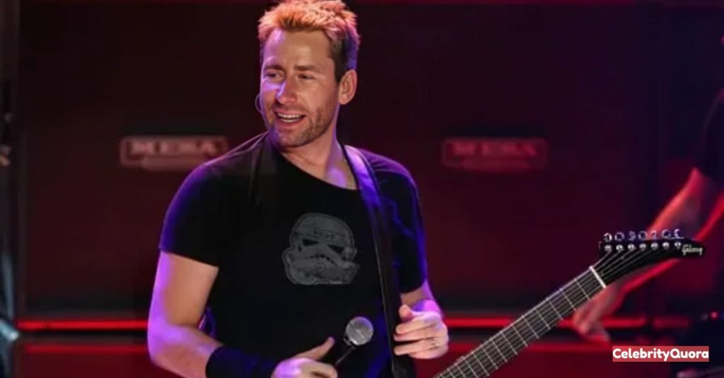 Chad Kroeger, the lead singer of Nickelback, performs on stage, holding a microphone and his electric guitar. He is smiling and has bleached blonde, spiky hair, wearing a black t-shirt with a Stormtrooper helmet graphic.