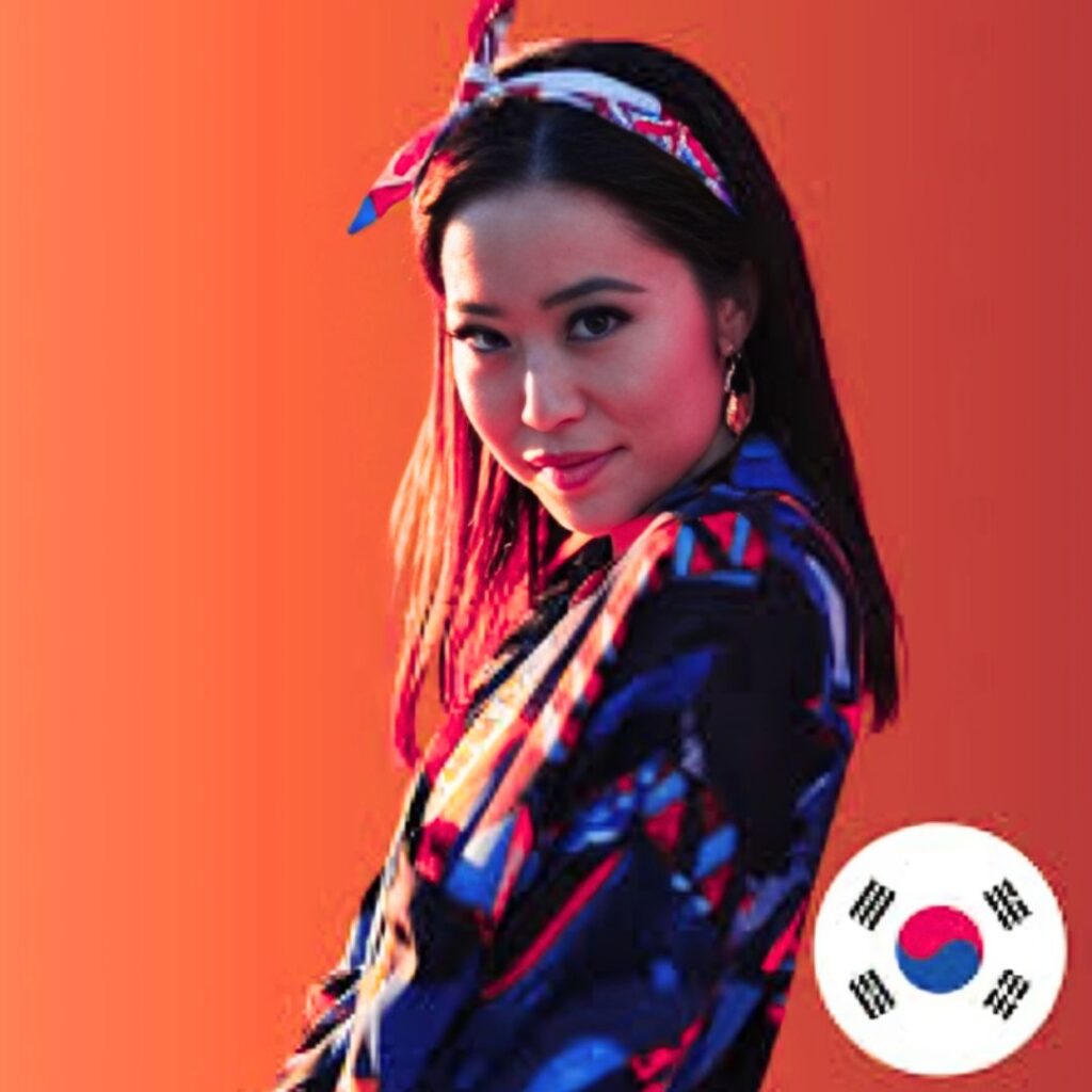 Stephanie Soo is wearing a colorful patterned jacket and a headband, looking over her shoulder at the camera with a slight smile. A circular South Korean flag icon is in the bottom right corner of the image.