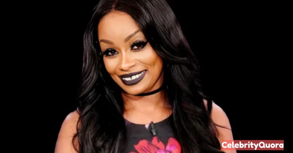 A headshot of Tokyo Toni smiling, with a black background. She has long dark hair and is wearing a black floral top and a black choker necklace.