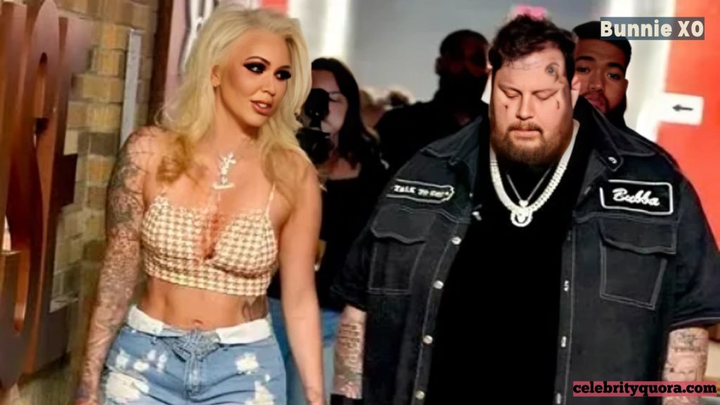 Bunnie XO with her husband, the musician Jelly Roll, walking together. She is wearing a crop top and ripped jeans, and he is in a black denim jacket and a black t-shirt.