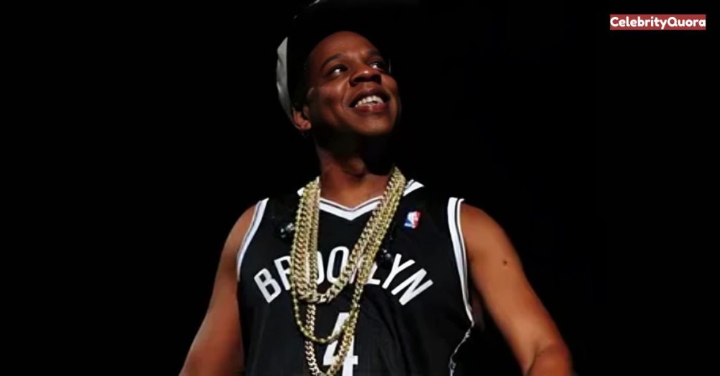 Jay-Z performing on stage, wearing a Brooklyn Nets jersey and multiple gold chains.