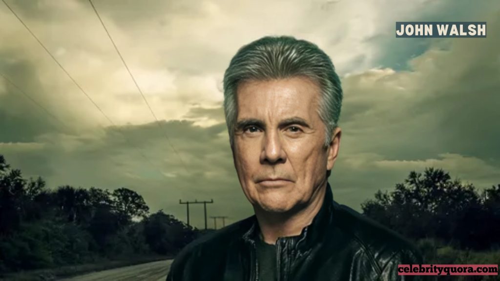 A close-up shot of John Walsh outdoors, with a cloudy sky and power lines in the background. He is wearing a black jacket and has a serious expression.