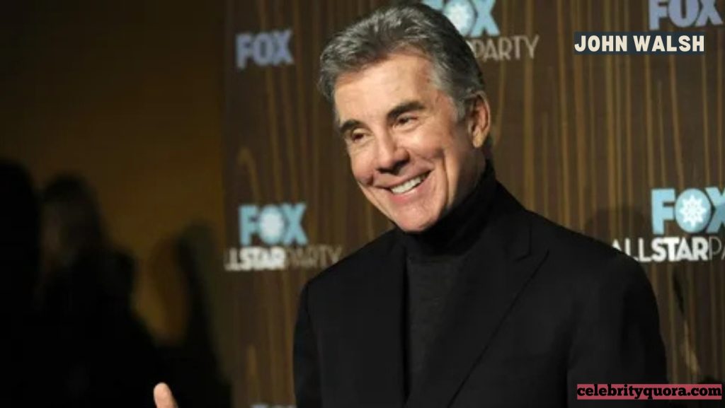 John Walsh standing in what appears to be a warehouse or industrial setting, looking directly at the camera with a serious expression. He is wearing a dark jacket.