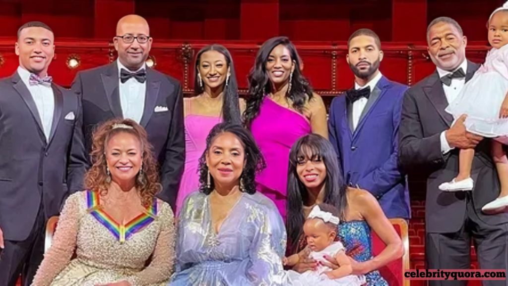  Debbie Allen and her extended family, including her sister Phylicia Rashad, posing together in formal wear against a red theatrical background, featuring adults and young children.